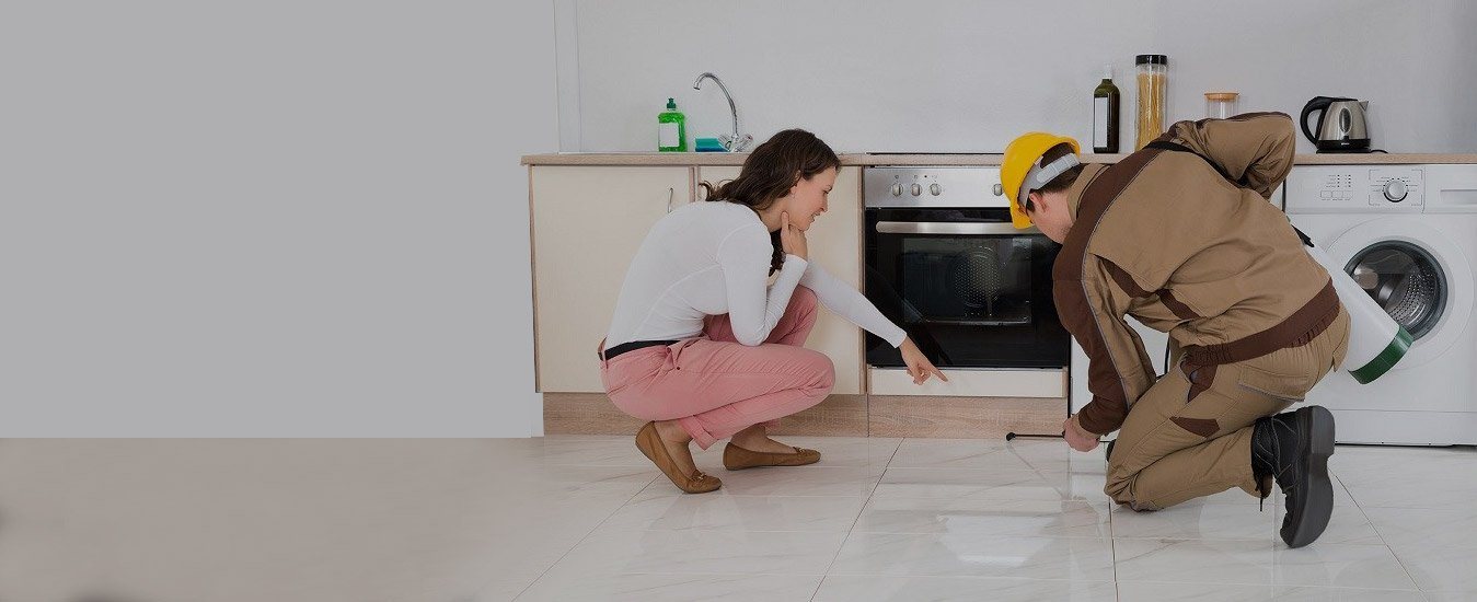 Pest control technician inspecting under kitchen cabinets while the homeowner watches